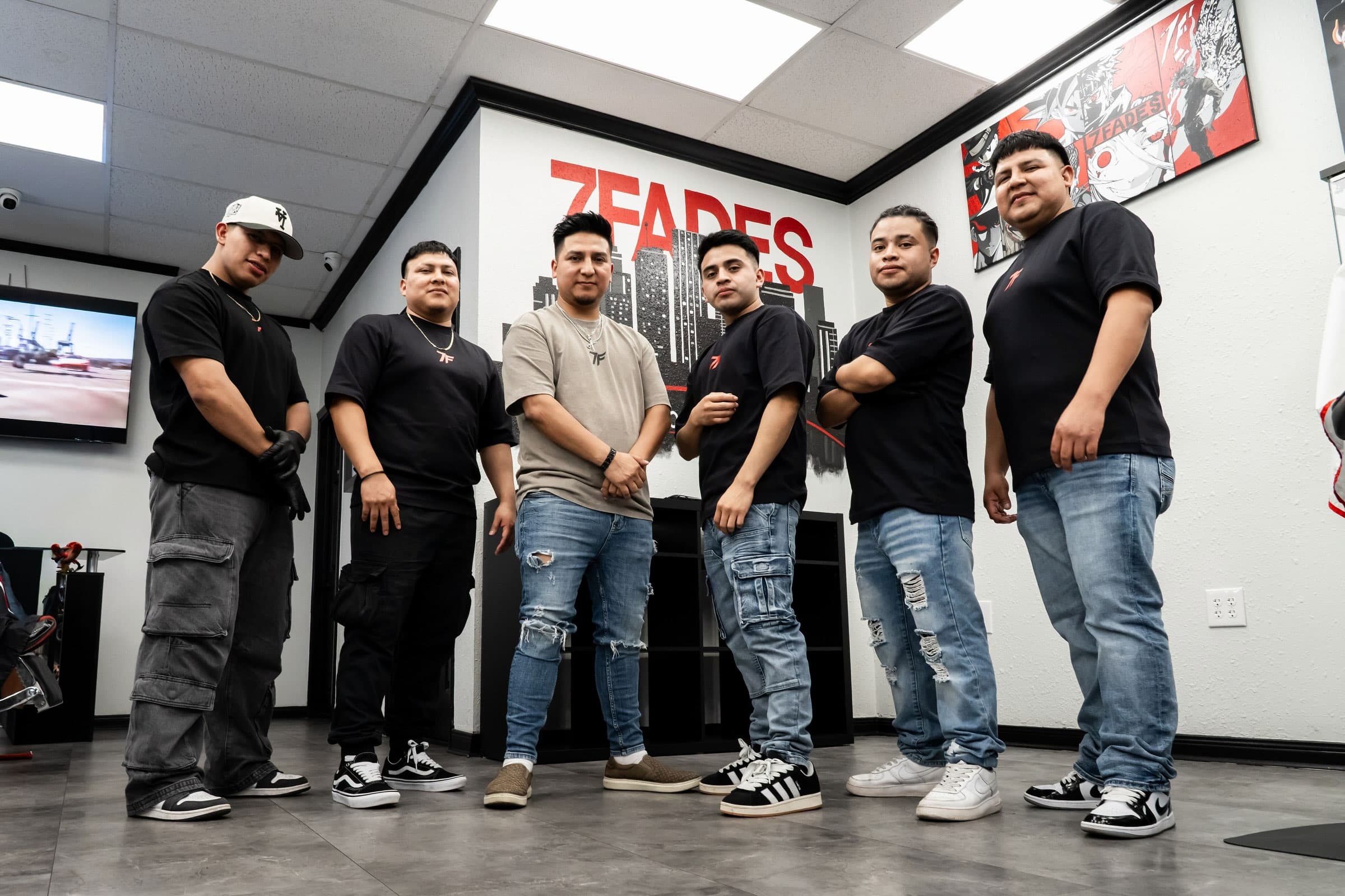The 7Fades barbershop team inside the Bellaire shop in front of the Houston skyline mural and anime art